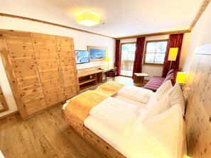 Une chambre d’hôtel avec un grand lit, une armoire en bois, un bureau avec une chaise, une télévision et une fenêtre avec des rideaux.