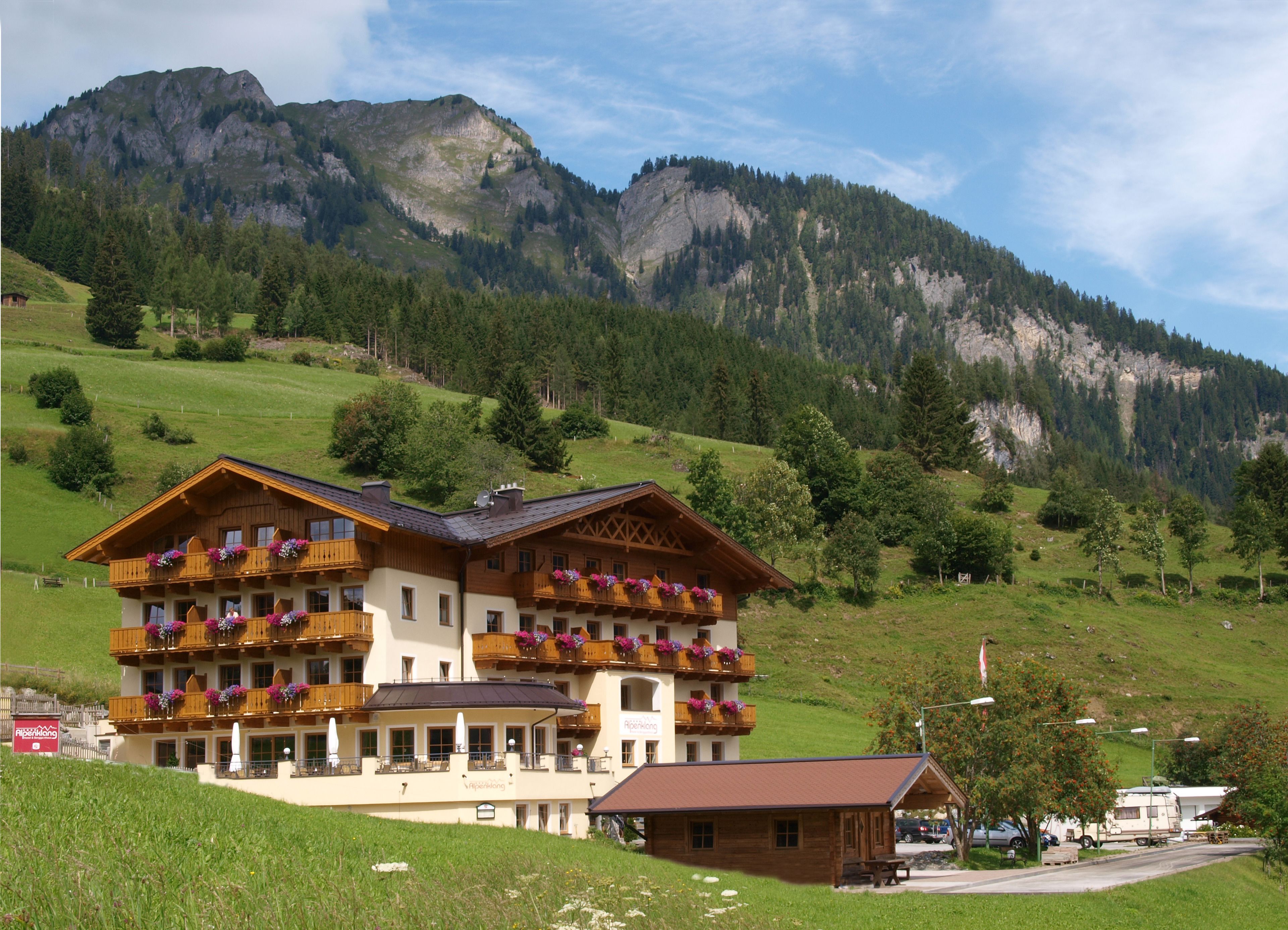 A chalet-style hotel with multiple balconies, a covered outdoor seating area, and a view of a mountainous landscape.