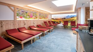 Un cuarto de spa con paredes de madera, sillones reclinables rojos, un ventanal con vistas a la montaña y una zona de bar de madera.