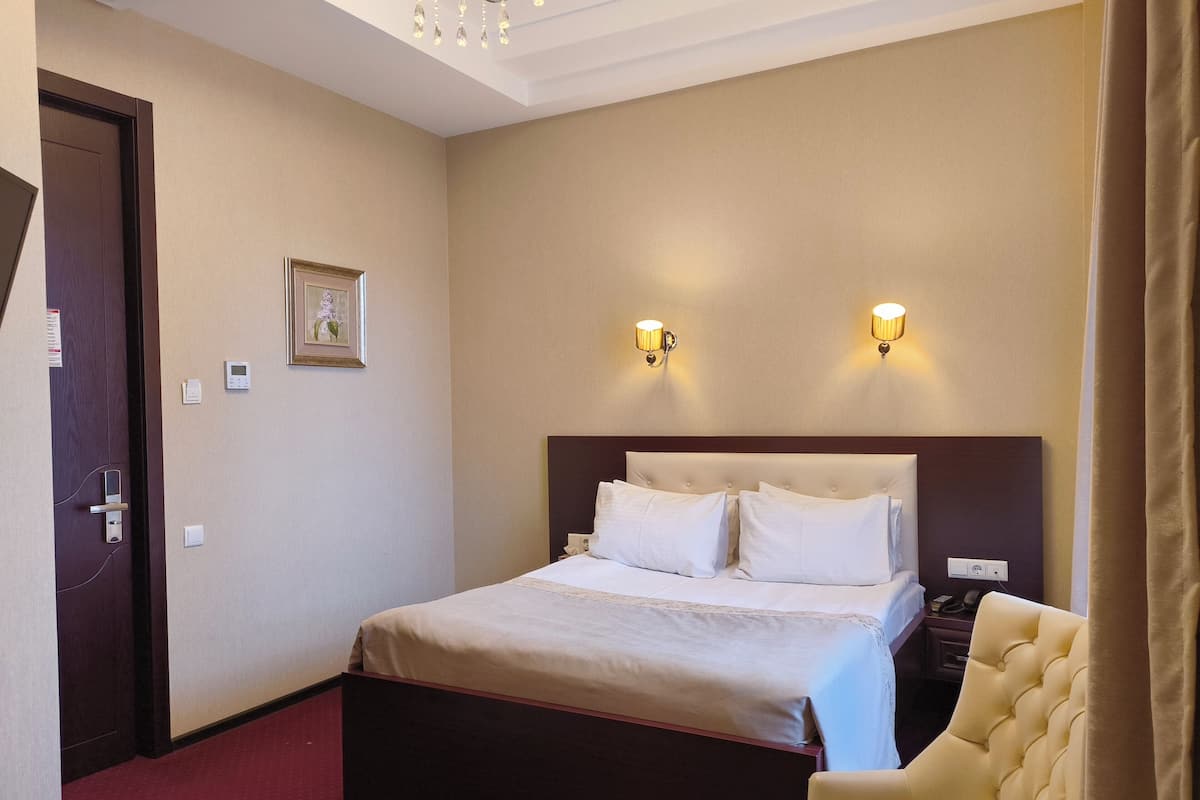 Een hotelkamer met een bed, nachtkastje, lamp en stoel.