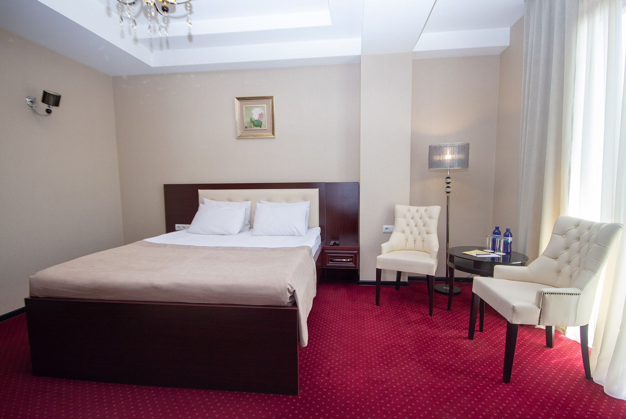 A hotel room with a large bed, a chair, a small table, and a lamp.