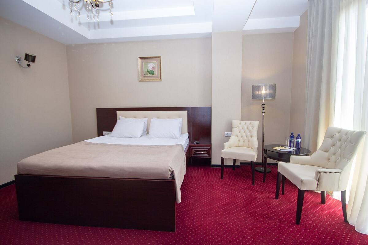 Een hotelkamer met een groot bed, een stoel, een tafeltje en een lamp.