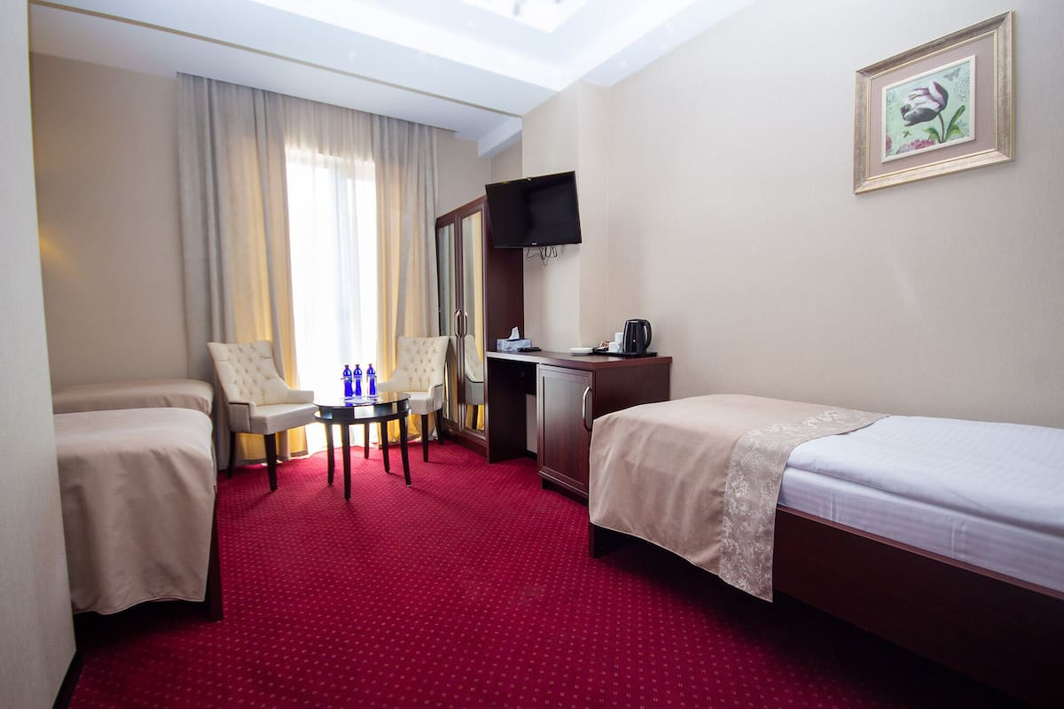 Een hotelkamer met twee enkele bedden, een bureau met stoel, een televisie en een raam met gordijnen.