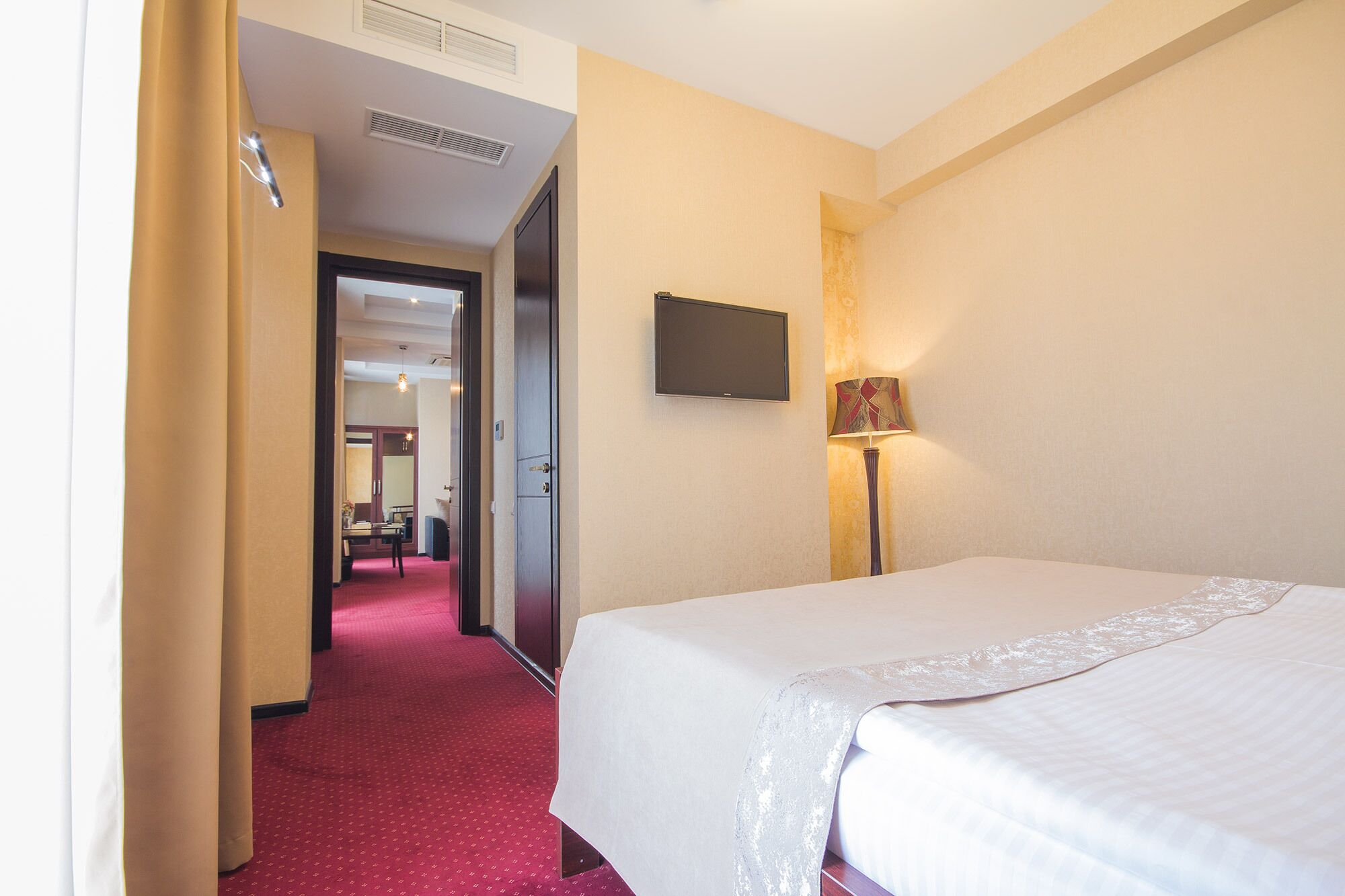 A hotel room with a bed, a television mounted on the wall, and a lamp.