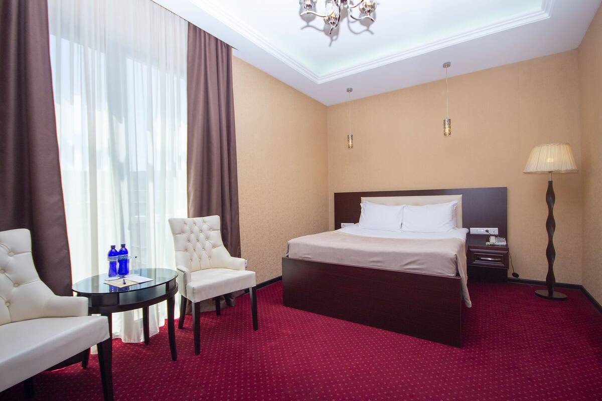Een hotelkamer met een bed, een stoel, een klein tafeltje, een lamp en een kroonluchter.