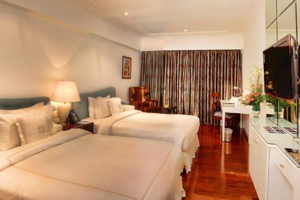 A hotel room with two beds, a desk, a chair, a TV, and a curtain.