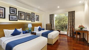 Quarto de hotel com duas camas, uma escrivaninha, uma cadeira, um abajur e quadros nas paredes.