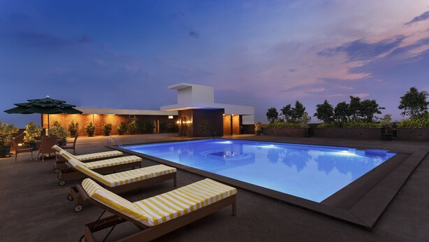 A modern outdoor pool area with lounge chairs and a building in the background. - La Marvella, Bengaluru (Bengaluru)