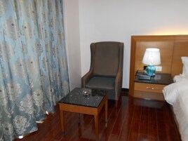 A hotel room with a wooden floor, a small table with a lamp, a chair, and a bed with a headboard.