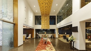 A hotel lobby with a central reception desk, a red carpet, and a high ceiling with a golden decorative element. - La Marvella, Bengaluru (Bengaluru)