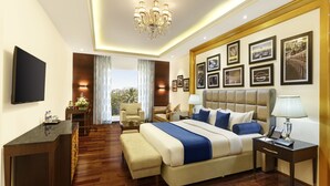 A spacious bedroom with a large bed, a desk, and a chair, a chandelier, and framed pictures on the wall. - La Marvella, Bengaluru (Bengaluru)