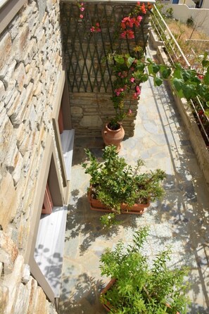 A stone wall with a metal gate, potted plants, and a tiled patio area. - Rastoni Apartments (Andros)