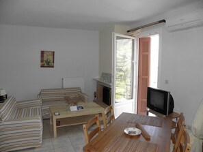A cozy living room with a sofa set, a wooden table, a television, and a fireplace. - Rastoni Apartments (Andros)