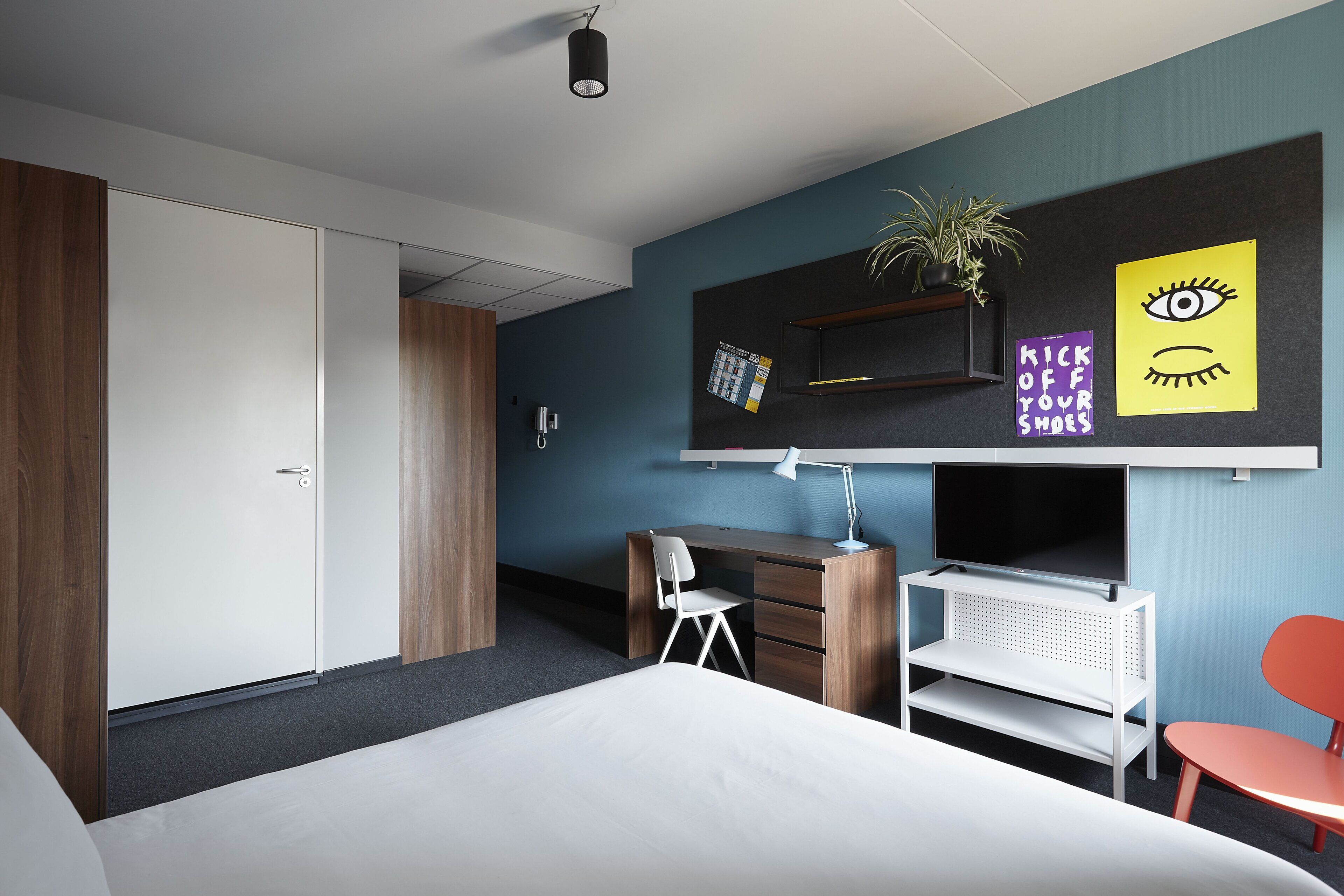 A modern bedroom with a bed, a desk, a chair, and a TV.