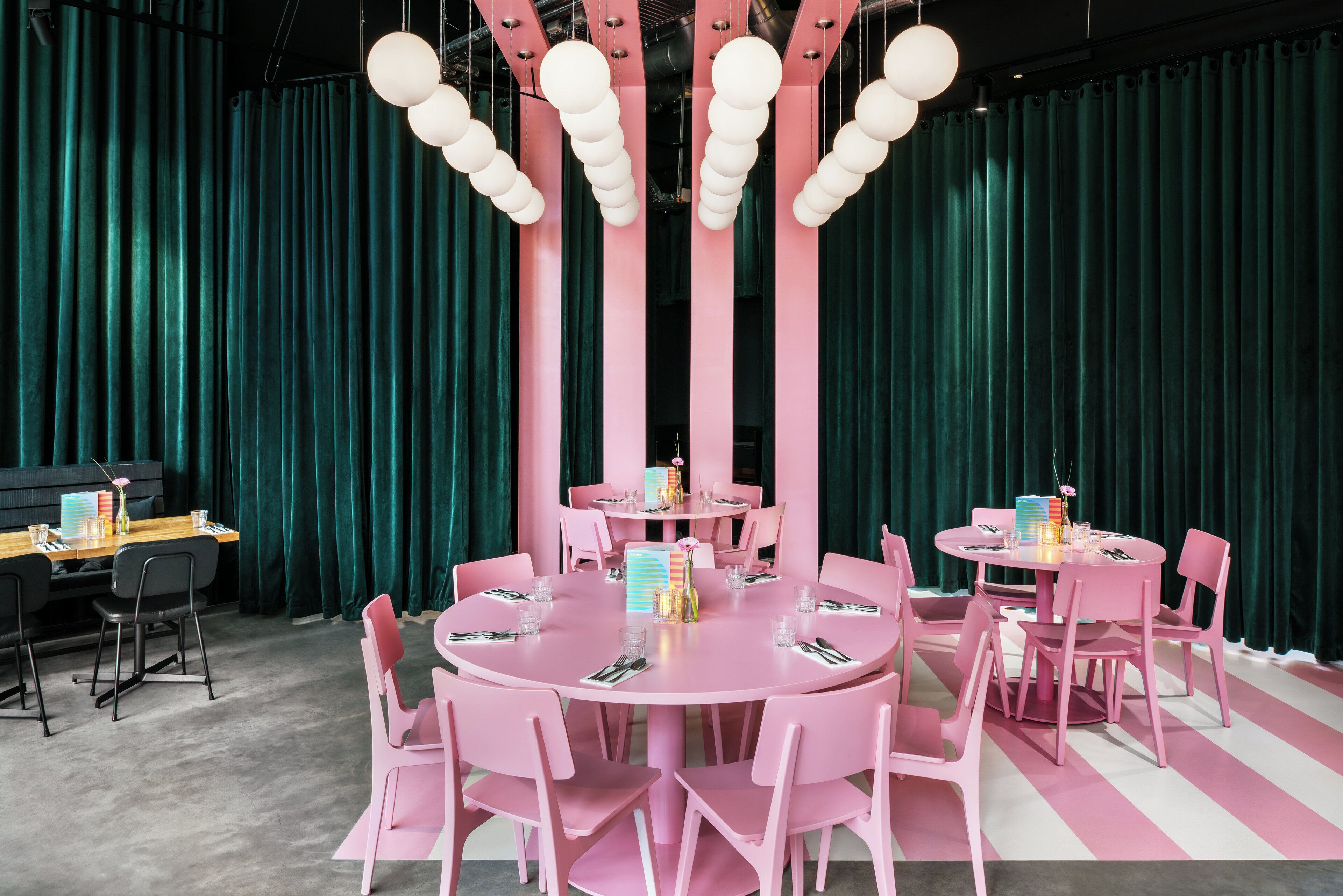 A room with two round tables, pink chairs, and teal curtains.