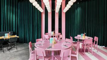 A room with two round tables, pink chairs, and teal curtains.