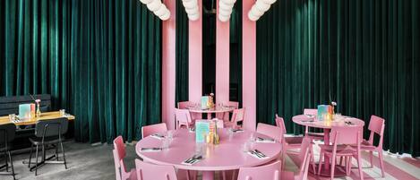 Una habitación con dos mesas redondas, sillas rosadas y cortinas color turquesa.
