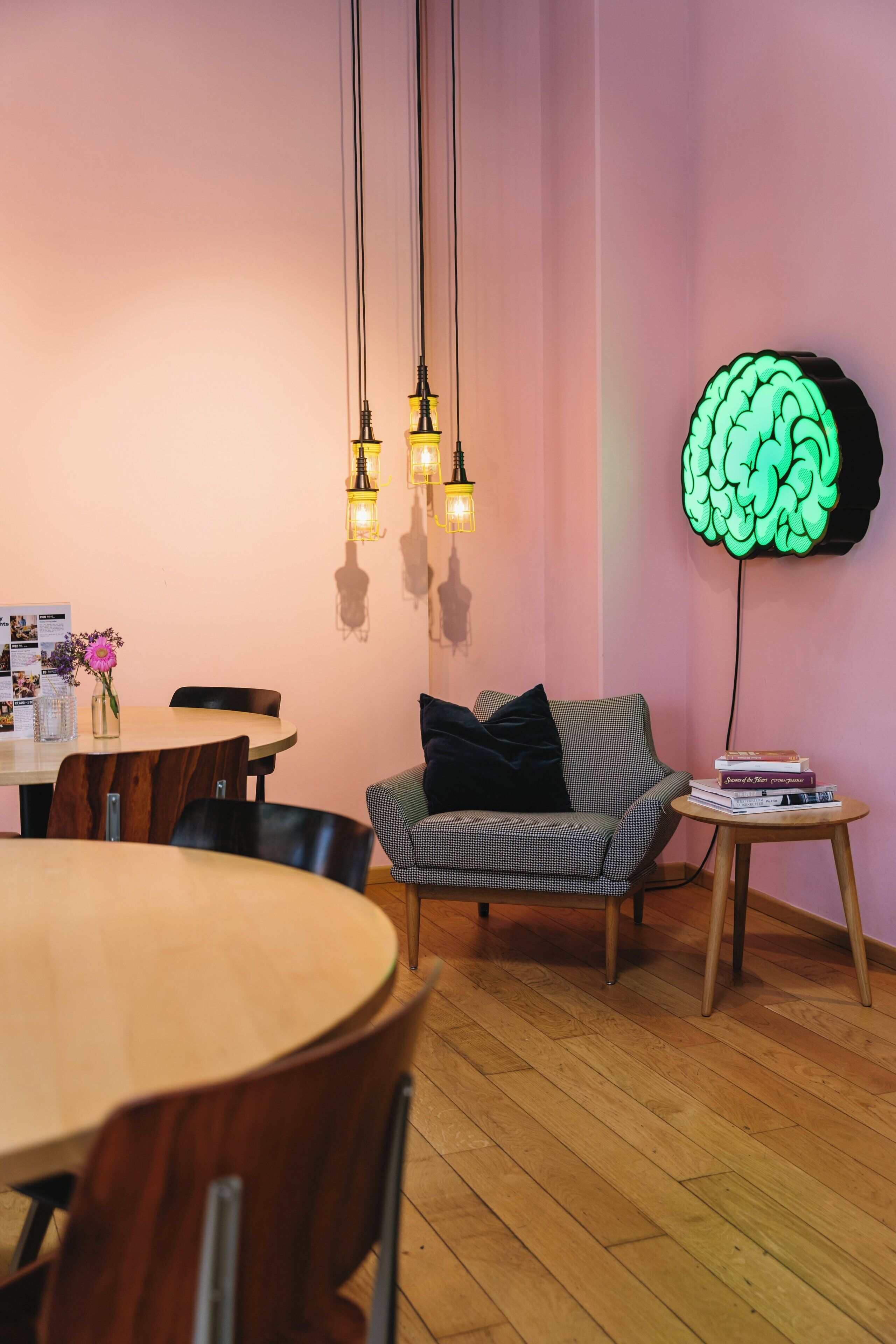Um quarto aconchegante com uma mesa de jantar de madeira, um sofá xadrez e um luminária em formato de cérebro fixada na parede.