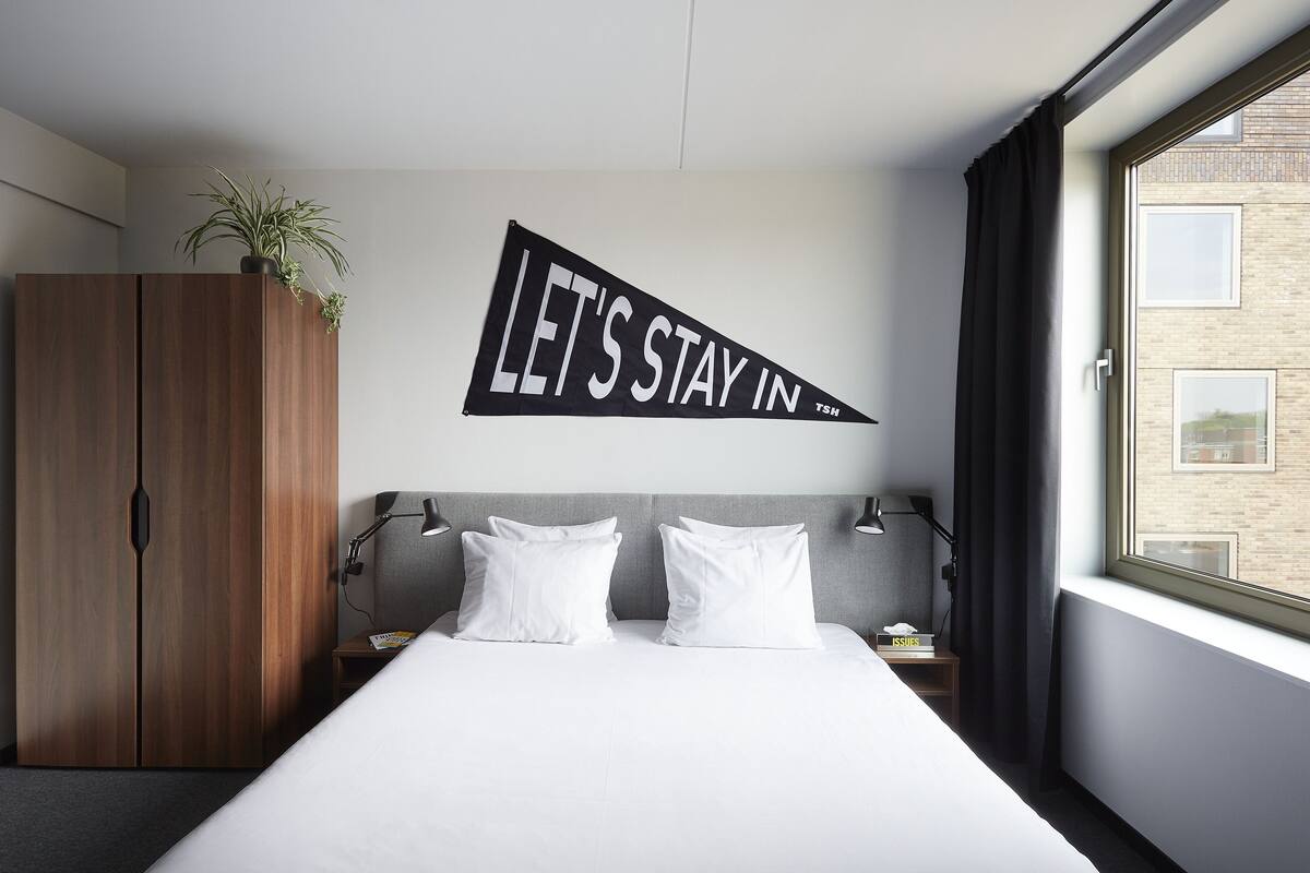 A hotel room with a bed, a wardrobe, a wall-mounted sign, a window, and a view of a building.