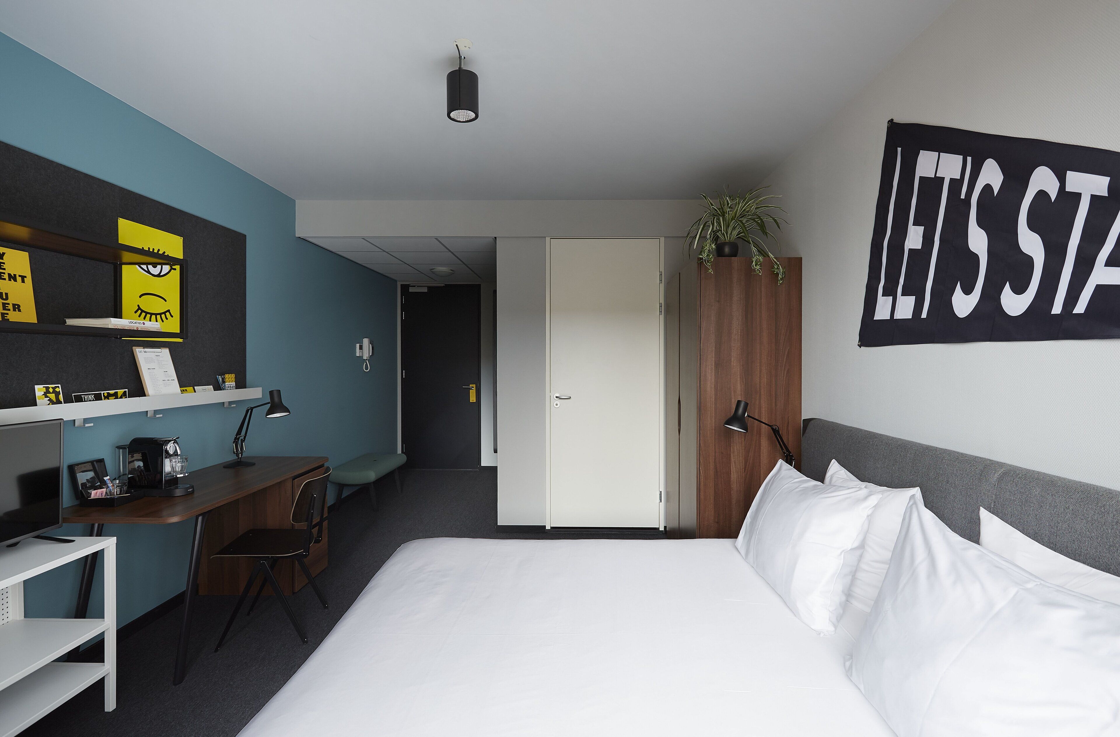 A hotel room with a bed, desk, chair, and a wall with a sign.