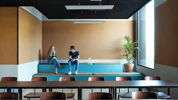 A modern conference room with a long table, wooden chairs, a bench seating area, and a large window.