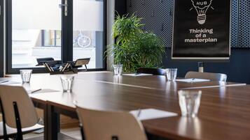 A conference room with a long table, chairs, a potted plant, and a poster on the wall.
