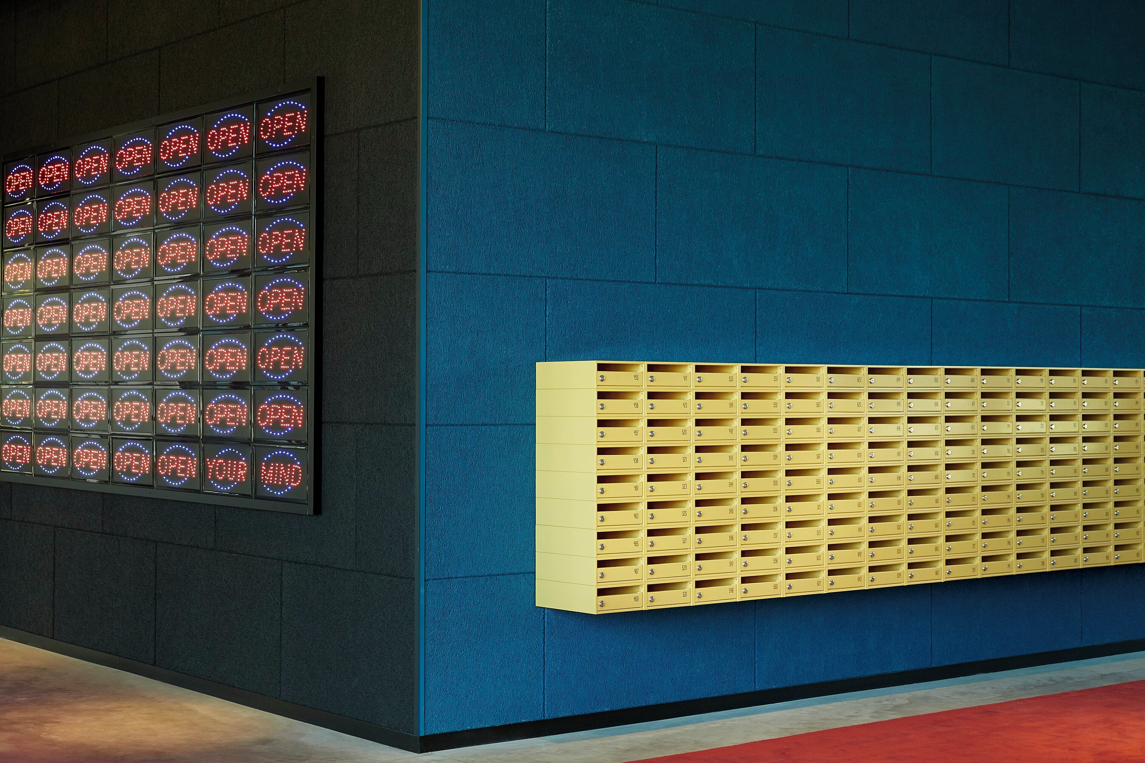 Een muur met een blauw paneel en een rij gele brievenbussen.