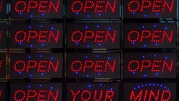 A series of illuminated signs with the word "OPEN" in red letters, and one sign with "OPEN YOUR MIND" in red letters.