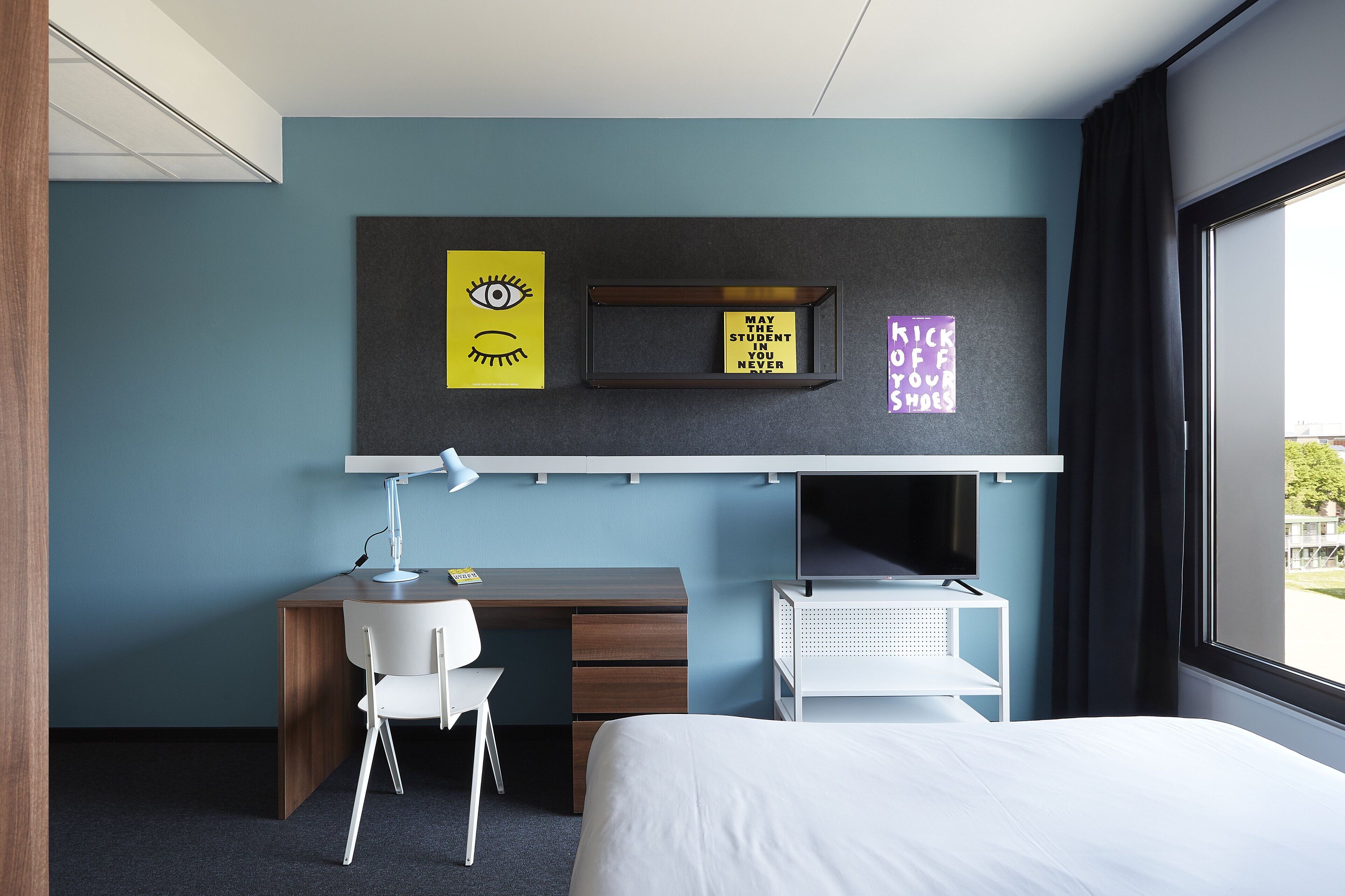 A hotel room with a desk, chair, bed, and a window with curtains.