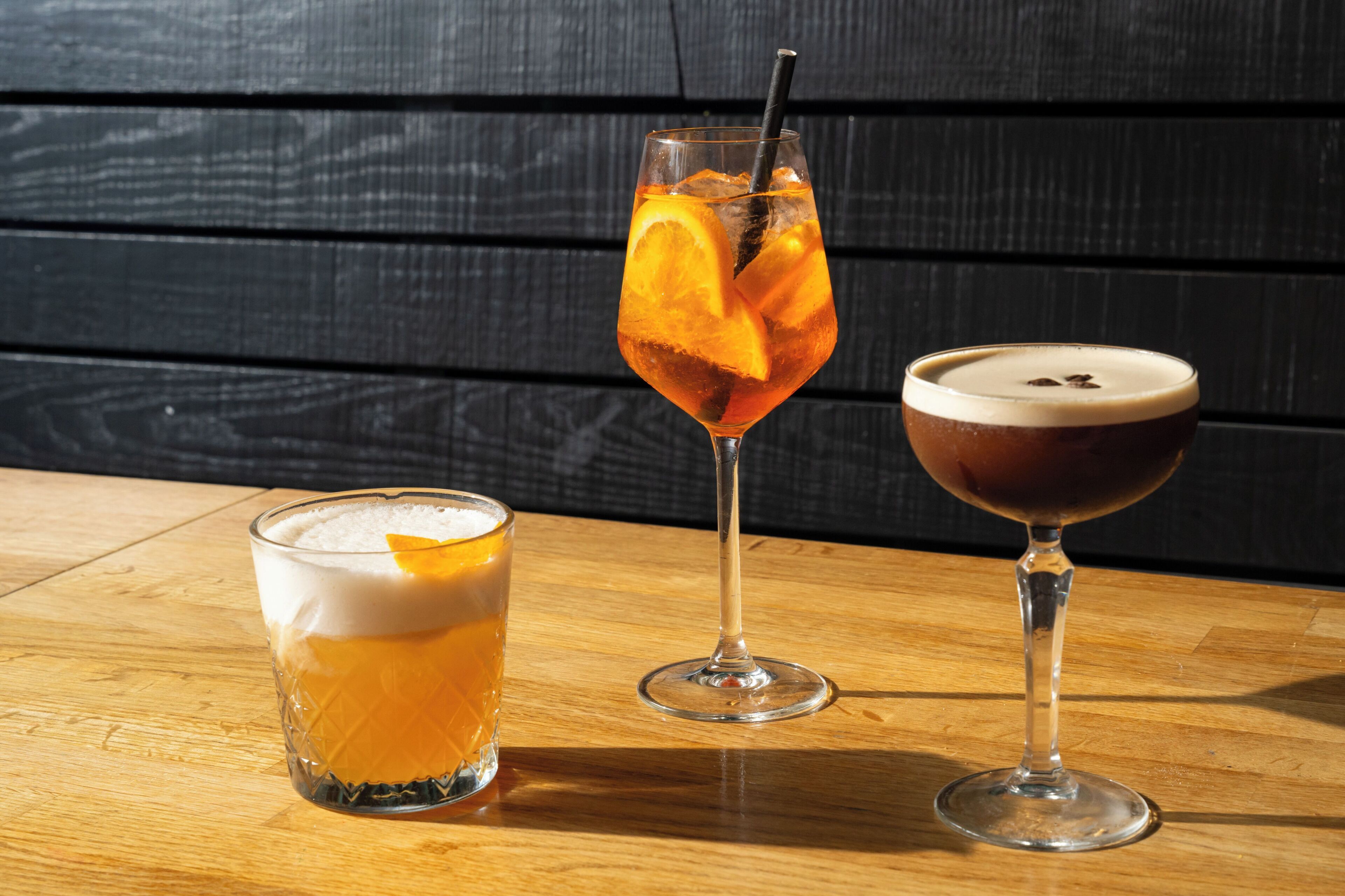 Three glasses of beverages on a wooden table against a dark wooden backdrop.