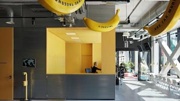 Un espace d’accueil avec un bureau jaune, une personne assise derrière, et une grande fenêtre laissant entrer la lumière naturelle.