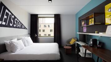 Hotelkamer met een groot bed, een bureau met stoel, een raam met gordijnen en een muur met motiverende posters.