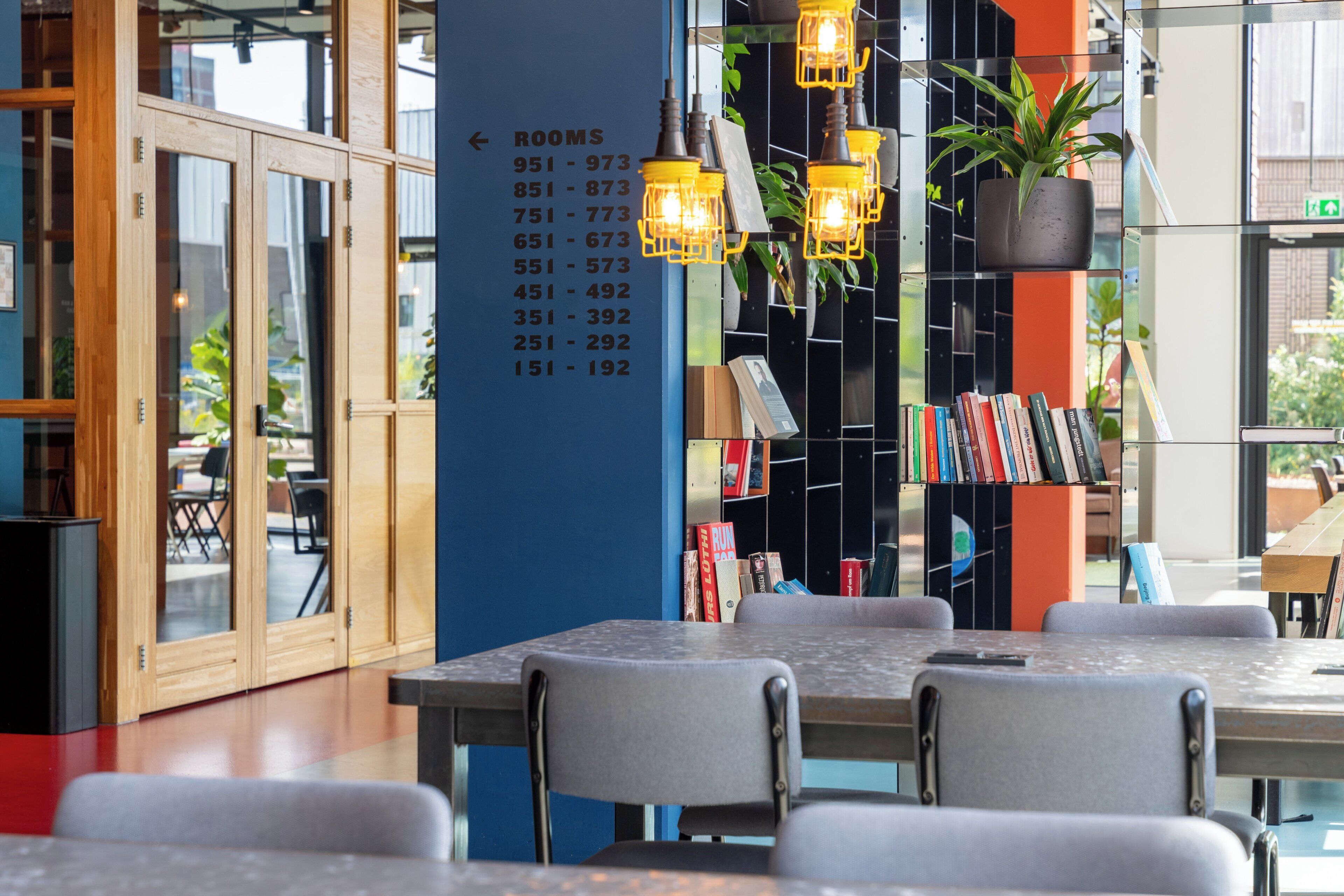 A modern interior with a room number sign, tables, chairs, and a potted plant.