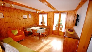 A wooden cabin interior with a green sofa, orange armchair, dining table, and chairs. - Chalet Alpenruh (Saas-Fee)