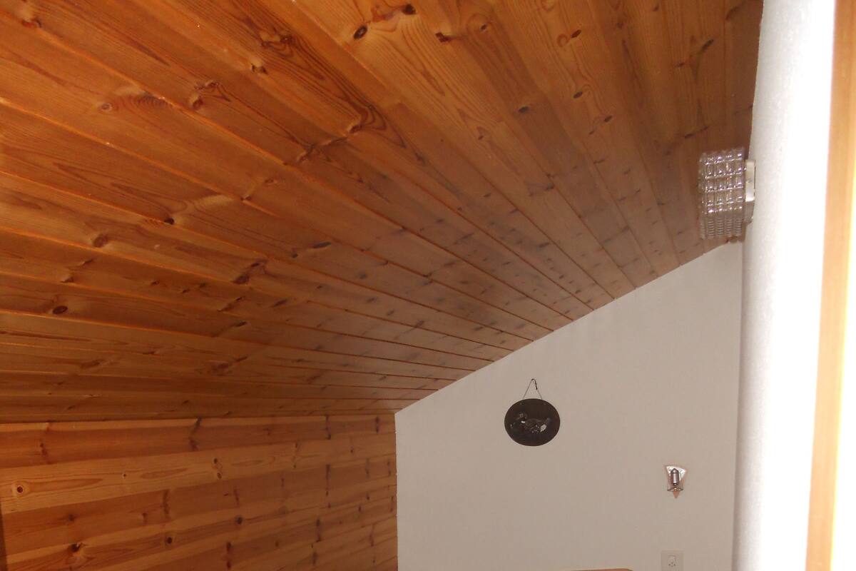 A small, single-bed room with wooden walls and a sloped ceiling.