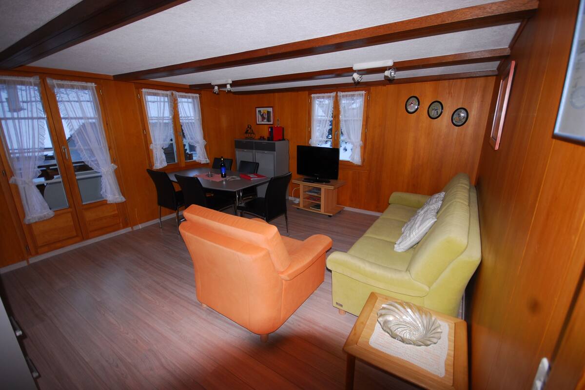 A compact living area with a dining table, orange and yellow sofas, a television, and a small cabinet.