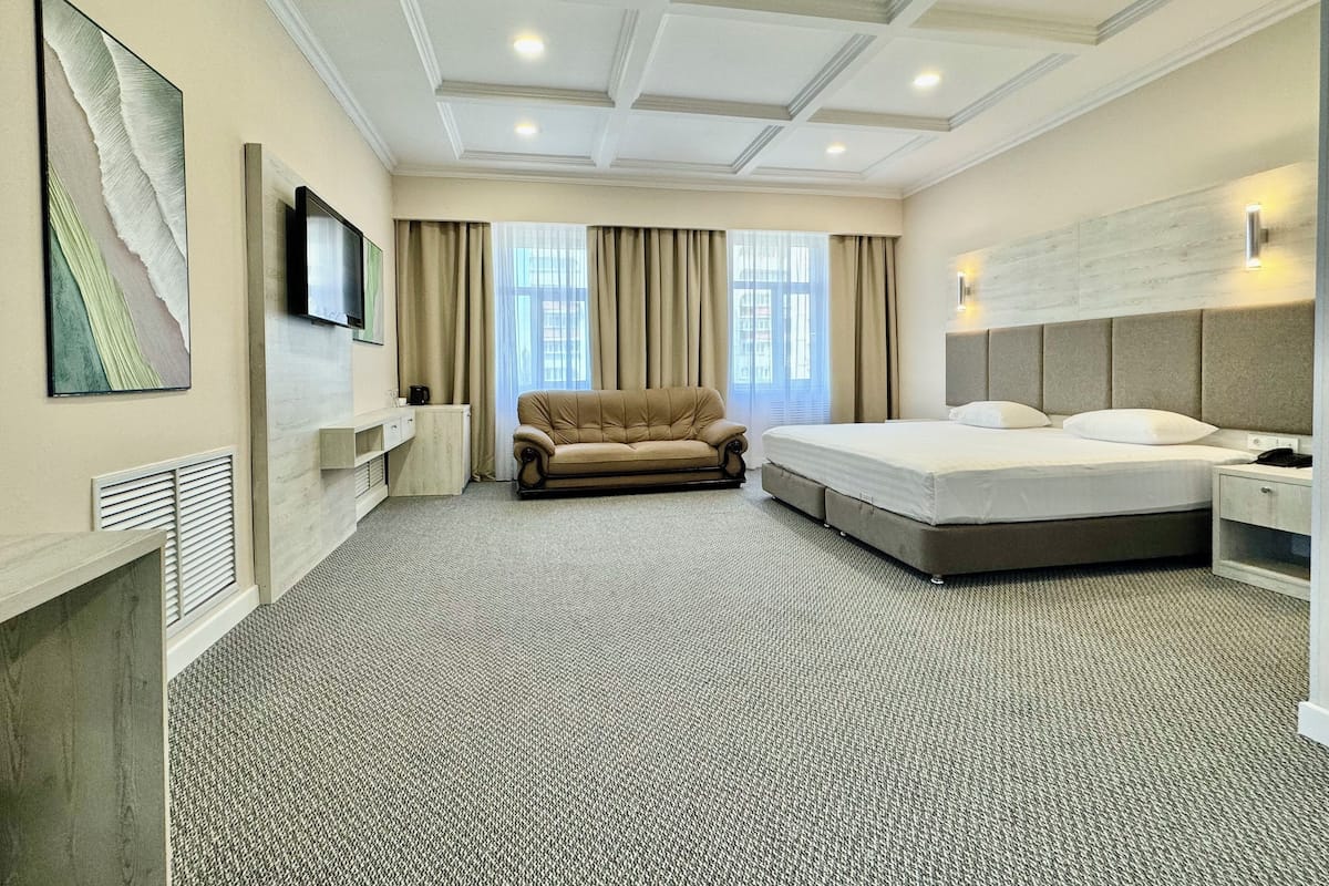 A hotel room with a large bed, a sofa, a TV, and a window with curtains.