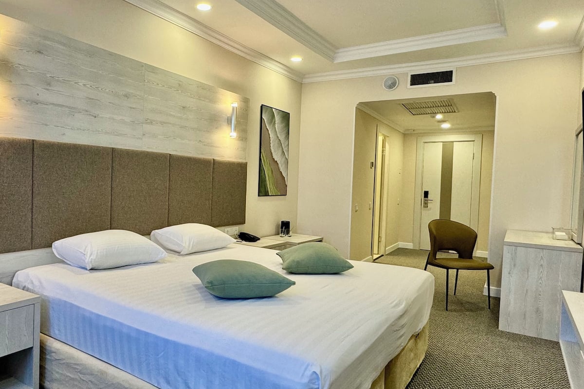 A hotel room with a large bed, a nightstand, a desk, a chair, and a painting on the wall.