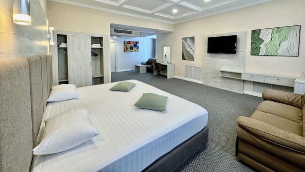 Quarto de hotel com uma cama grande, um sofá, uma TV e um closet espaçoso.