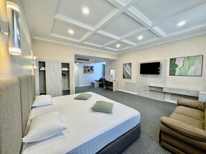 A hotel room with a large bed, a sofa, a TV, and a walk-in closet. - Grand Hotel Eurasia (Almaty)