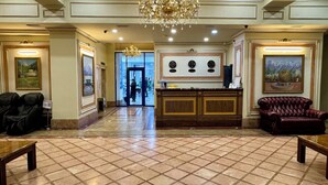 Um hall de entrada com uma receção, um candelabro, um sofá de couro e obras de arte emolduradas nas paredes.