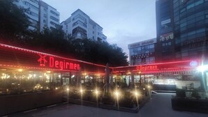 Um restaurante chamado Degirmen com área externa e letreiros de neon vermelhos.