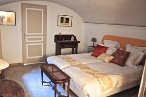 Ein Schlafzimmer mit Bett, Bank, Nachttisch, Lampe und Tür.