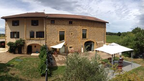 A two-story stone house with a tiled roof, a covered patio with outdoor seating, and a small garden area. - Le Clos du Cher en Beaujolais (Saint-Germain-Nuelles)