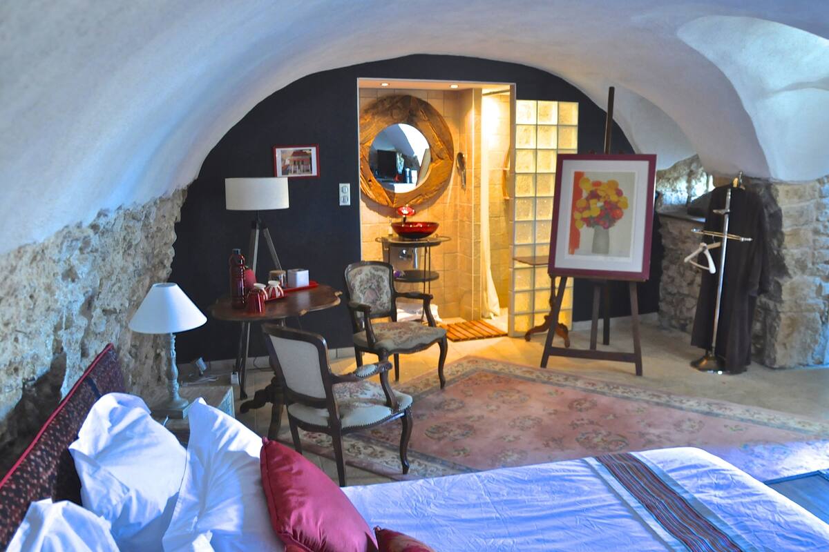 A cozy room with a bed, a desk, a chair, a round mirror, and a painting on the wall.