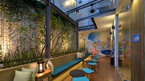 An indoor seating area with a low wall, wooden tables, and benches. - POP! Hotel Pasar Baru Jakarta (Jakarta)