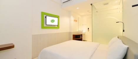A hotel room with a bed, a bedside table, a mirror, and a wall-mounted TV.