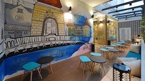 A café with a mural of a cityscape, tables, and chairs. - POP! Hotel Pasar Baru Jakarta (Jakarta)