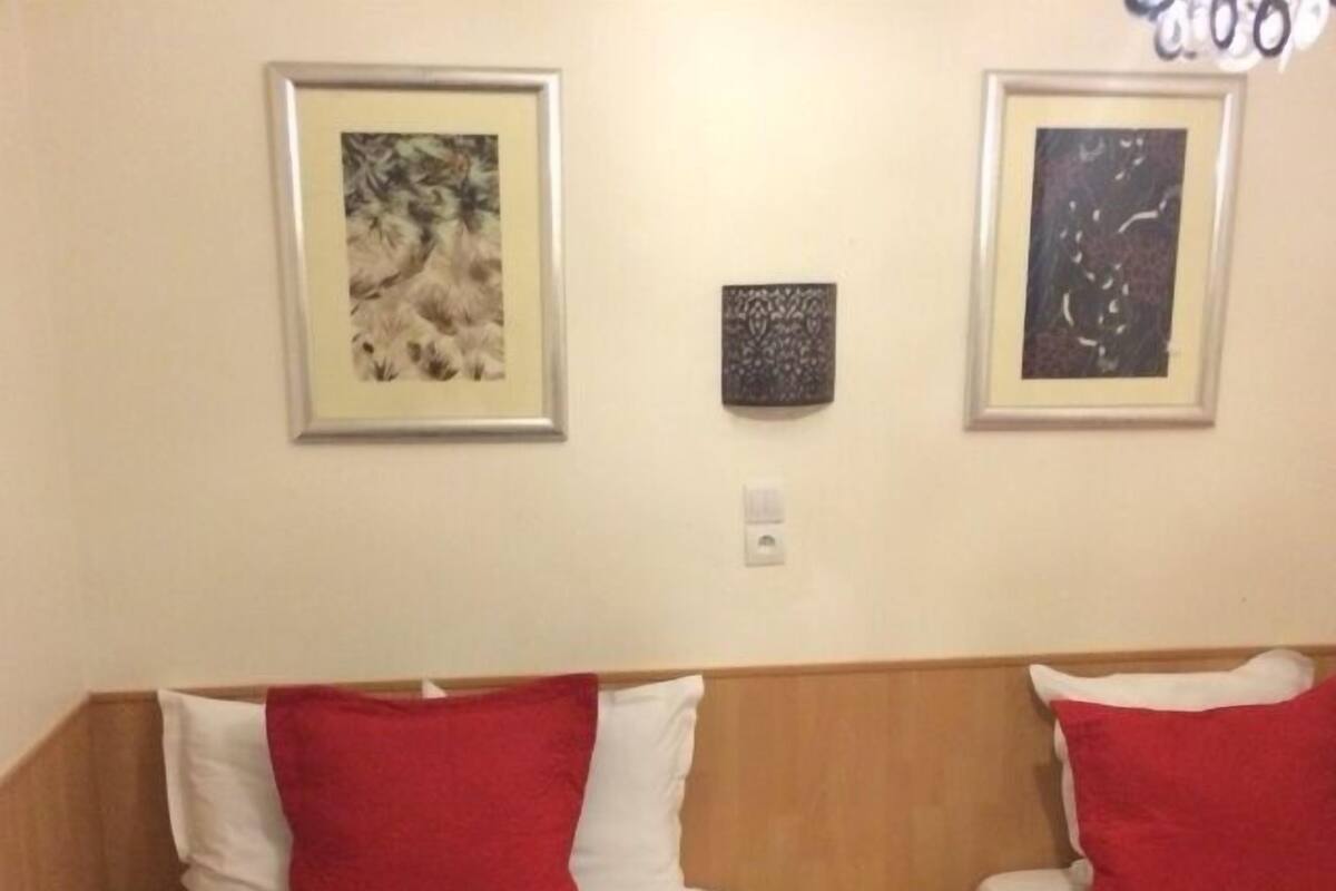 A hotel room with two beds, each with a red and white pillow, and a wooden headboard. There are framed artworks on the walls.