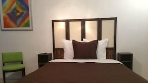 A hotel room with a large bed, a green chair, two bedside tables, and a colorful painting on the wall. - Hôtel Nice Savoie (Nice)